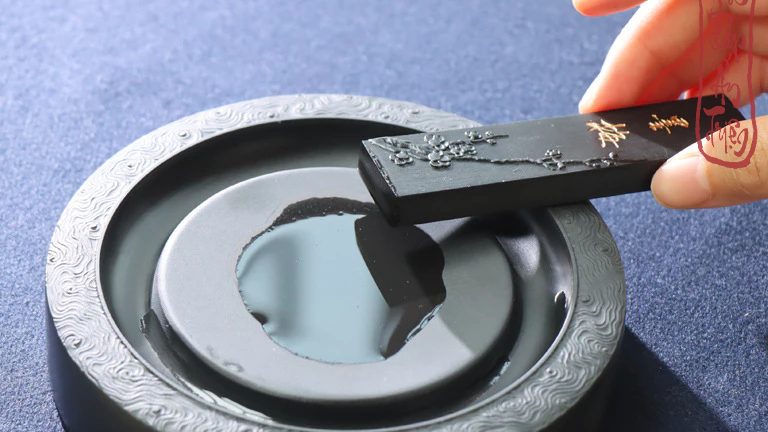 Bàn tay cầm thỏi mực đen trên nghiên tròn